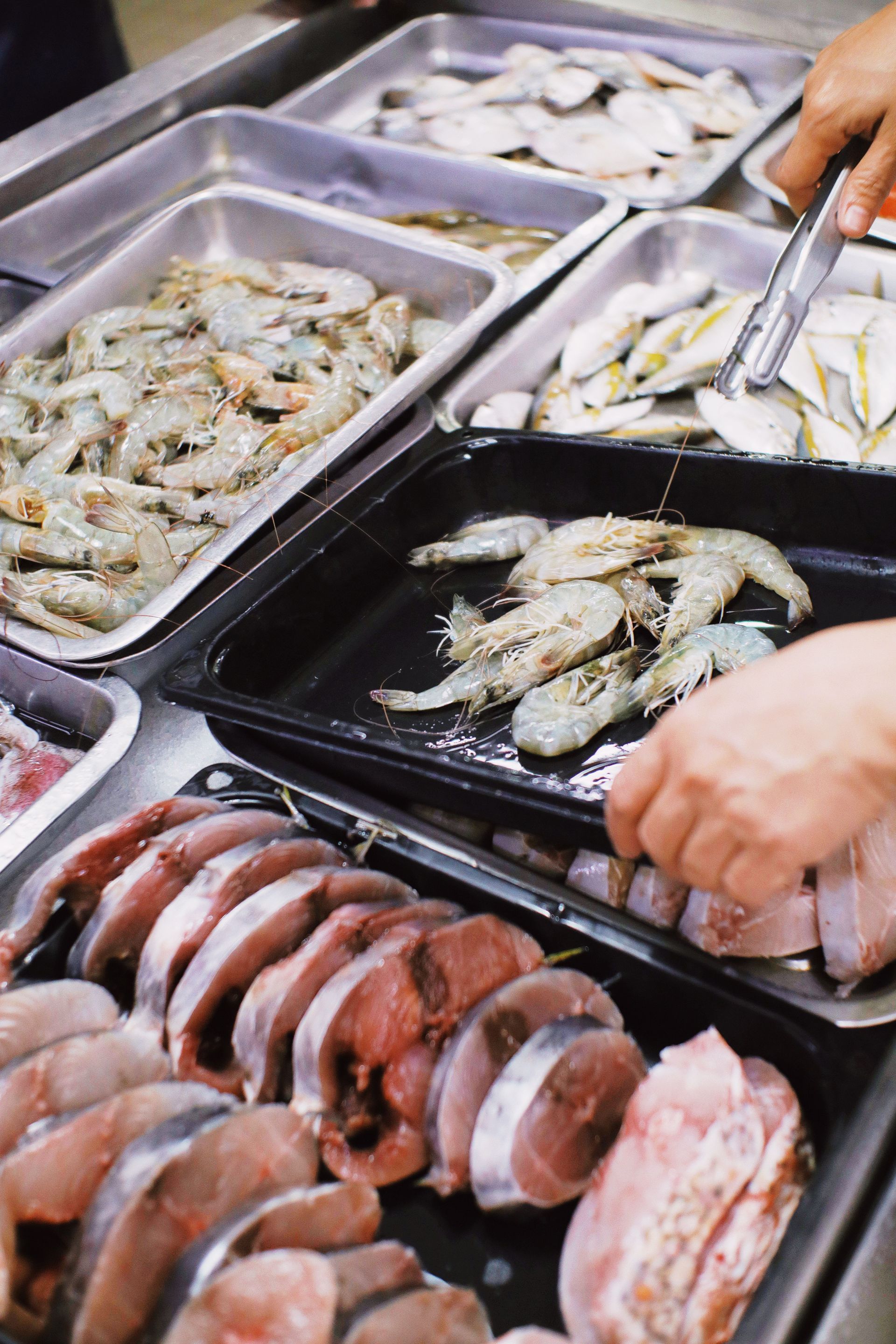 From above of crop anonymous seller putting fresh prawns in plastic container in local market